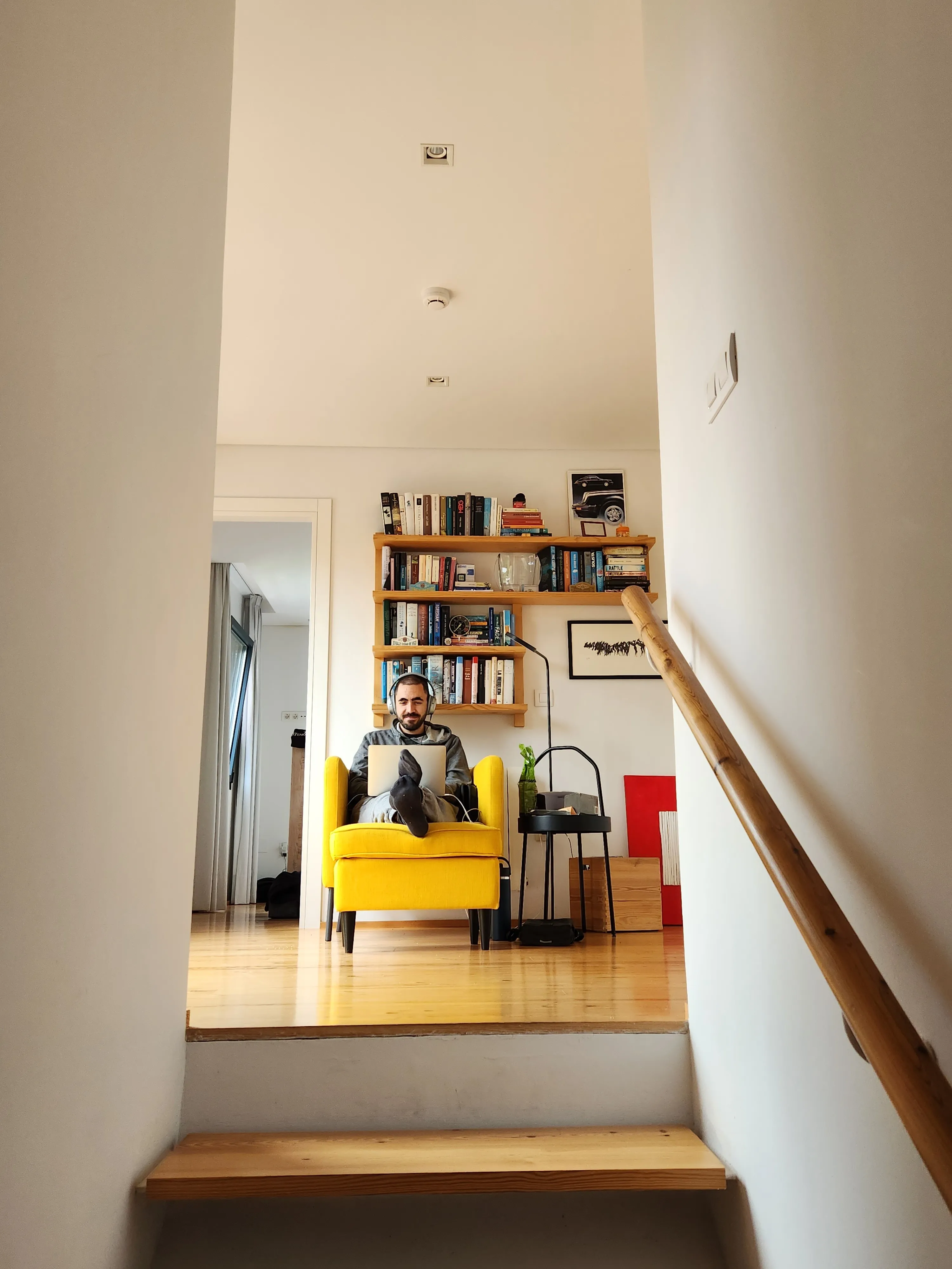 João Saraiva, founder of Postopus, working on a laptop in a yellow armchair in front of a bookshelf